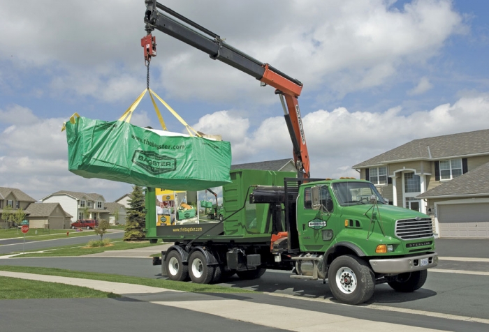 A truck hauling a Bagster away from a home